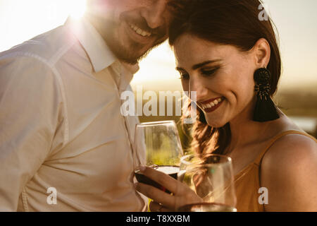 7/8-schuss ein glückliches Paar zusammen lachen Holding Glas Rotwein. Seitenansicht der ein lächelndes Paar auf einem romantischen Wein Datum. Stockfoto