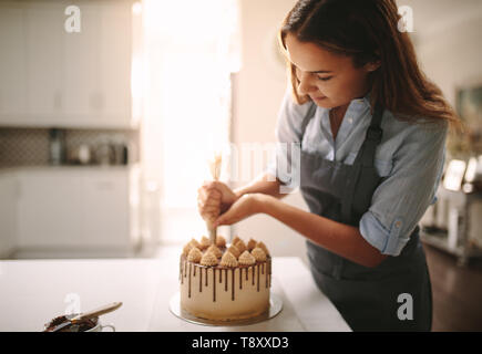Frau verzieren Schokolade Kuchen in der Küche. Frau Koch, einen Kuchen zu Hause. Stockfoto
