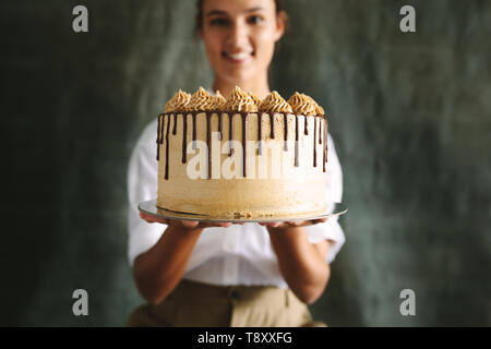 Weibliche baker Holding einen leckeren Kuchen. Koch Holding frisch gebackenen Kuchen gegen grauen Hintergrund. Stockfoto