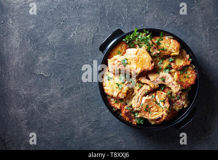 Lecker gebräunt Schweinekoteletts auf den Knochen- und Hash Brown Kasserolle in einem schwarzen Keramik pan auf einer konkreten Tabelle, horizontale Ansicht von oben, flach, s kopieren Stockfoto