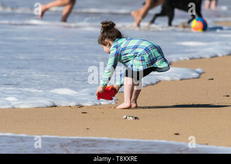 Ein Kleinkind, die versucht, ihr Eimer mit Meerwasser, ohne sich die Füße nass auf den Fistral in Newquay in Cornwall zu füllen. Stockfoto