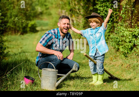 Bewässerung von Pflanzen. happy Earth Day. Stammbaum nursering. Vater und Sohn in Cowboy Hut auf Ranch. kleiner Junge Kind helfen Vater in der Landwirtschaft. Gießkanne, Topf und Schaufel. Gartengeräte. Eco Farm. Stockfoto