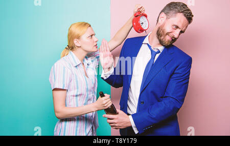 Nach Corporate Partei. Man Alkoholkrank. Böse Frau treffen betrunkenen Ehemann spät zu Hause. Geschäftsmann mit Alkohol Flasche und Frau mit Wecker. Süchtig Alkoholismus und Alkoholmissbrauch. Stockfoto