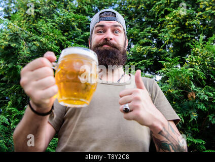 Daumen hoch für die besten Bier. Mann Trinker holding Bierkrug. Bärtiger Mann genießen Sie Bier trinken auf die Natur. Brutale Hipster mit langen Bart in Handwerk Bier. Stockfoto