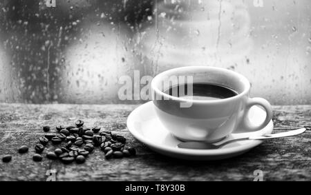 Herbst Wetter besser mit Koffein trinken. Genießen Kaffee an regnerischen Tag. Kaffee morgen Ritual. Frisch gebrühter Kaffee weiß Tasse und Bohnen auf Fensterbank. Nasses Glas Fenster und heiße Tasse Kaffee. Stockfoto