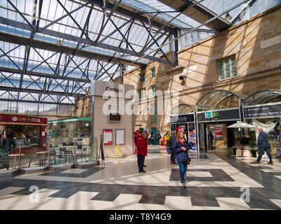Passagiere in Carlisle Railway Station an einem sonnigen Nachmittag, mit der Shops im Hintergrund Stockfoto