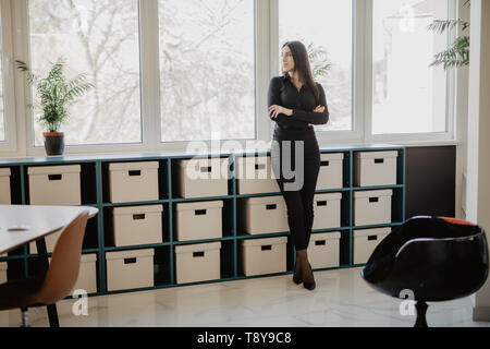 Lächelnd business stehende Frau mit verschränkten Armen im Amt. Frau in der Kleidung, der vor ihr steht Schreibtisch im Büro. Stockfoto