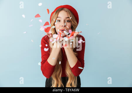 Portrait von Pretty Woman 20 s mit langen Haaren Holding und blasen Konfetti während über blauen Hintergrund im Studio isoliert Stockfoto