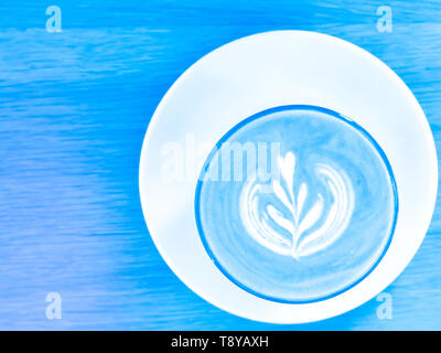 Heiße Milch Kaffee auf weißem Glas platte Holztisch Hintergrund blau Ton lifestyle Konzept Idee Stockfoto