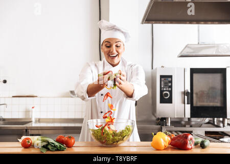 Foto der schönen Frau Koch tragen weiße Uniform, Salat mit frischem Gemüse in der Küche im Restaurant Stockfoto