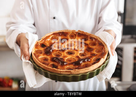 Das Bild der jungen Frau Koch tragen weiße Uniform holding Apfelkuchen beim Kochen in der Küche in der Bäckerei Stockfoto