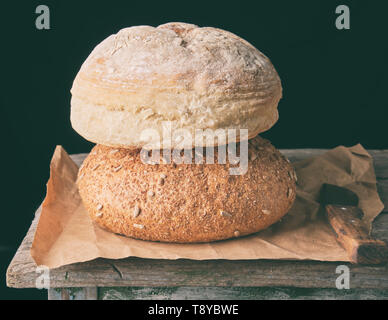 Zwei Brote gebacken runde Brot legen auf braunem Papier, schwarzer Hintergrund Stockfoto