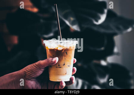 Hand halten Eis Kaffee in ein hohes Glas mit Sahne über und Kaffeebohnen auf einer Natur Grün verlassen dunklen Ton gegossen. Kalten Sommer trinken Hintergrund Stockfoto