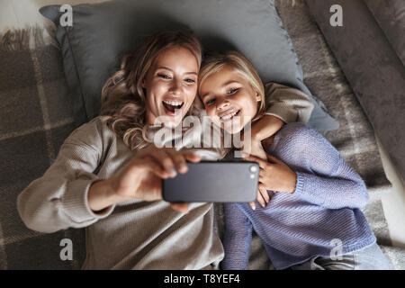 Bild einer glücklichen jungen Frau mit ihrer kleinen Schwester zuhause zu Hause nehmen eine selfie per Handy. Stockfoto