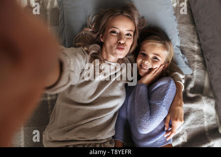 Bild einer glücklichen jungen Frau mit ihrer kleinen Schwester zuhause zu Hause nehmen eine selfie durch die Kamera. Stockfoto