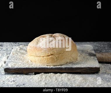 Runde gebackenes Brot und weißes Mehl von Weizen auf einem hölzernen Tisch verstreut, schwarzer Hintergrund Stockfoto