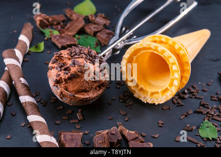 Schokoladeneis in Schaufel mit wafer Sticks, Kegel und Schokolade auf schwarzem Schiefer. Fokus auf Eis in Schaufel. Stockfoto