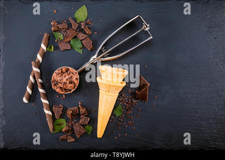 Schokoladeneis in Schaufel mit wafer Sticks, Kegel und Schokolade auf schwarzem Schiefer. Fokus auf Eis in Schaufel. Stockfoto