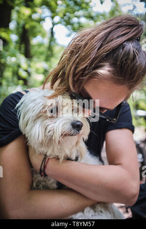 Brünette Frau mit Sonnenbrille ihr süsses Malteser Hund umarmt Stockfoto