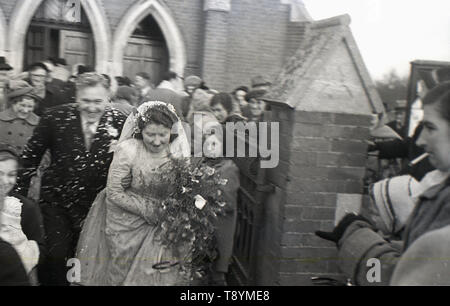 1950 s, historischen, nach der Hochzeit, Braut und Bräutigam dash für ihren Transport nach mit Feier conffetti vor den Toren der Kirche, England, UK. Stockfoto