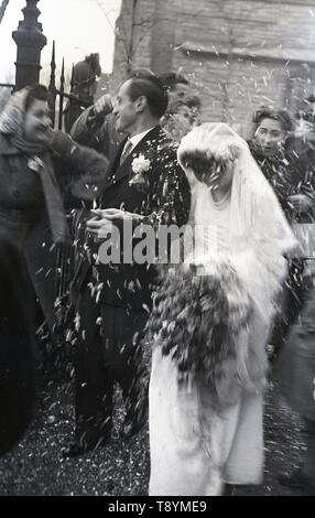 1950 s, historischen, nach der Hochzeit Service, sehen wir eine Braut und Bräutigam geduscht oder mit Konfetti durch die Gäste vor den Toren der Kirche geworfen, England, UK. Stockfoto
