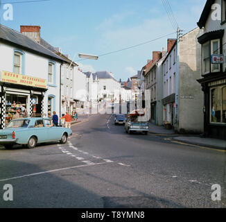 1960, historische Bild aus dieser Ära der St. Michael Straße, Brecon, Powys, Wales, in dem die Kammern Family Motor Parts Shop und ganz rechts, der M&B Boars Head Pub. Stockfoto