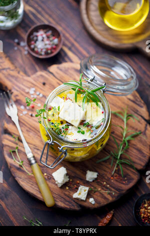 Feta Käse, mariniert in Olivenöl mit frischen Kräutern in Glas. Holz- Hintergrund. Stockfoto
