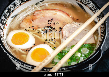 Japanische Ramen Suppe mit Udon Nudeln, Schweinefleisch, Eier und Schalotten auf dunklem Stein Hintergrund Stockfoto