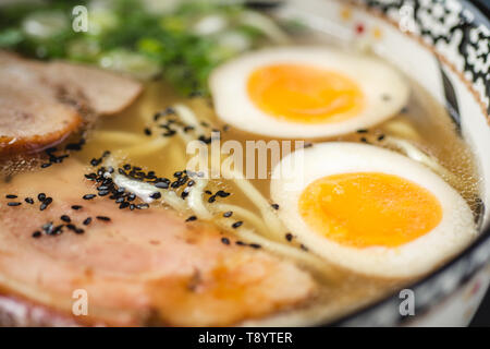 Japanische Ramen Suppe mit Udon Nudeln, Schweinefleisch, Eier und Schalotten auf dunklem Stein Hintergrund Stockfoto