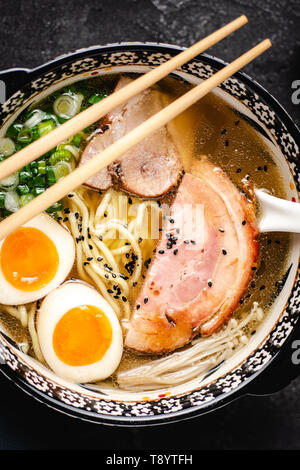 Japanische Ramen Suppe mit Udon Nudeln, Schweinefleisch, Eier und Schalotten auf dunklem Stein Hintergrund Stockfoto