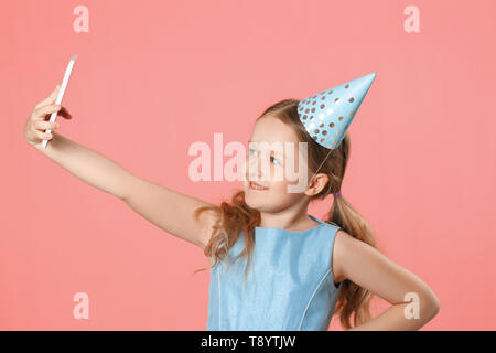 Fröhliches kleines Mädchen feiert Geburtstag. Das Kind hält das Telefon, nimmt eine selfie. Closeup Portrait auf rosa Koralle Hintergrund. Stockfoto