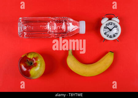 Gesunde Schule Essen. Konzept: Schule Essen. Schule Mittagessen eine Flasche mit reinem Wasser, ein Sandwich, einen Apfel und eine Uhr auf rotem Papier Hintergrund Stockfoto