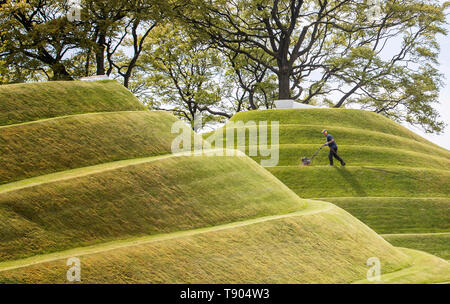 Gärtner das Gras auf die Zellen des Lebens Landschaftsformen durch Landschaftsarchitekt Charles Jeneks, einer der standortspezifischen Skulpturen auf dem Gelände des Jupiter Artland, Edinburgh erstellt mähen. Stockfoto