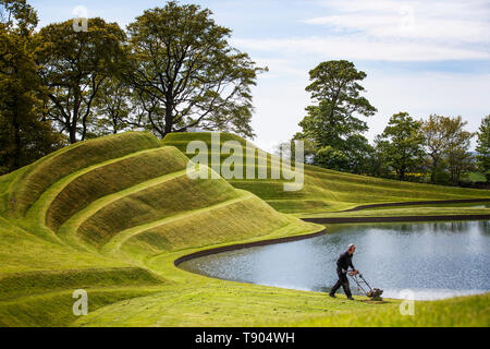 Gärtner das Gras auf die Zellen des Lebens Landschaftsformen durch Landschaftsarchitekt Charles Jeneks, einer der standortspezifischen Skulpturen auf dem Gelände des Jupiter Artland, Edinburgh erstellt mähen. Stockfoto