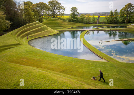 Gärtner das Gras auf die Zellen des Lebens Landschaftsformen durch Landschaftsarchitekt Charles Jeneks, einer der standortspezifischen Skulpturen auf dem Gelände des Jupiter Artland, Edinburgh erstellt mähen. Stockfoto