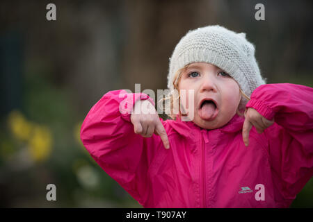 Kleine Mädchen in hat Gesichter ziehen in Garten Stockfoto