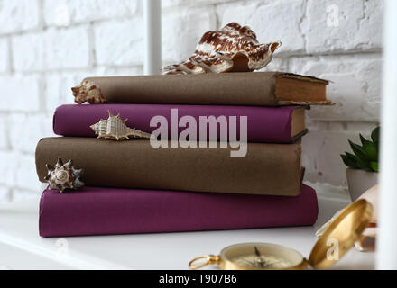 Stapel von Büchern und Muscheln auf dem Regal in der Nähe von White Brick Wall Stockfoto