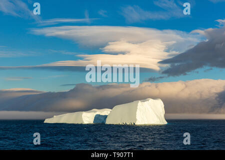 Eine spektakuläre eckig Eisberg aufgeteilt in zwei Hälften schwimmt unter einem Linsenförmigen Wolke von Elephant Island im Südlichen Ozean Stockfoto