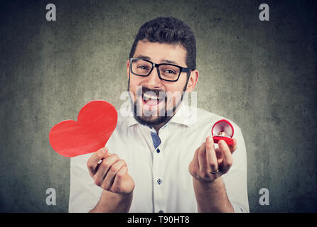 Super aufgeregt Mann mit roten Herzen Form Hochzeit Ring box. Romantische Vorschlag Konzept Stockfoto