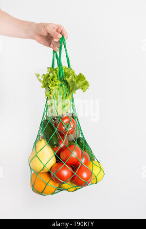 Netzbeutel von Obst, Gemüse, Grüns in der Hand der Frau. Null Abfall Konzept. Kunststoff frei. Vertikale erschossen. Weißer Hintergrund. Gesunde, Achtsamkeit Essen, Stockfoto