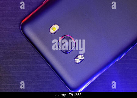 Ein Fragment der Cell Phone Case in Schwarz mit roter und blauer Hintergrundbeleuchtung. Das Telefon liegt auf dem Schwarzen technologische gerippte Oberfläche der Kamera nach oben Stockfoto