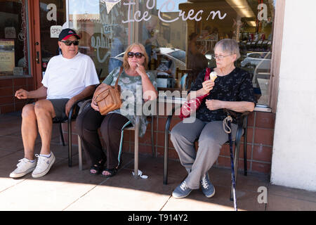 Drei Erwachsene, eine ältere männliche und zwei weibliche außerhalb eine Eisdiele in Ojai, Kalifornien sitzen. Die älteste weibliche isst ein Eis. Stockfoto