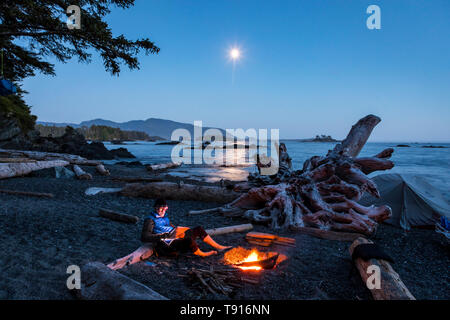 Ein einsamer Camper sitzt am Lagerfeuer auf einer kleinen Insel in Nuchatlitz Provincial Park British Columbia, Kanada Stockfoto