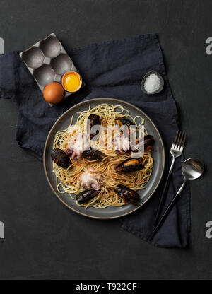 Mediterran Pasta mit Meeresfrüchten, Oktopus und Muscheln in graue Platte mit Geschirr, Servietten, Salz und Ei in der Nähe von auf dunklem Hintergrund. Konzept der Italienischen f Stockfoto
