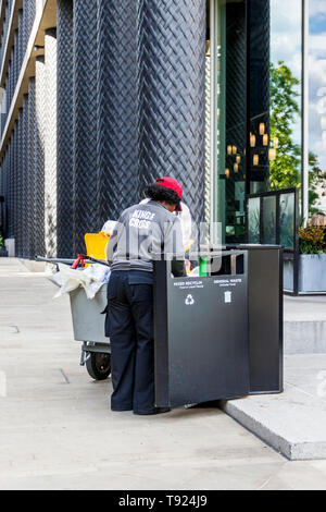 Ein weiblicher Rat Straße Reinigungsmittel mit einem Trolley Entleerung ein Mülleimer in Pancras Square, King's Cross, London, UK Stockfoto