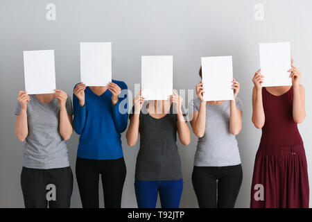 Junge Frauen ausblenden Gesichter hinter leeren Blatt Papier auf hellen Hintergrund Stockfoto