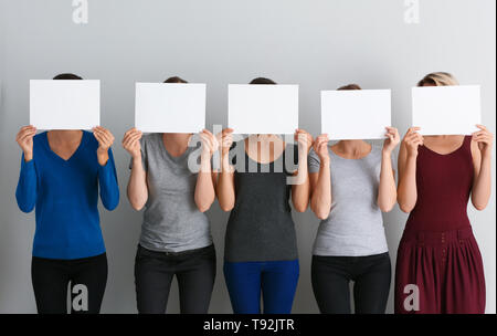 Junge Frauen ausblenden Gesichter hinter leeren Blatt Papier auf hellen Hintergrund Stockfoto