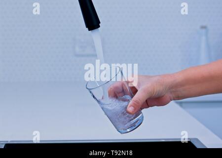 Füllen Sie ein Glas mit Wasser aus einer schwarzen Küche tippen. Stockfoto