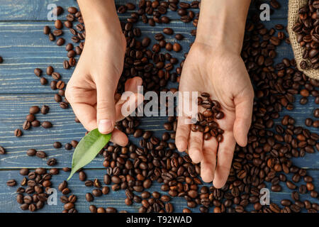 Weibliche Hände mit Kaffeebohnen auf hölzernen Hintergrund Stockfoto