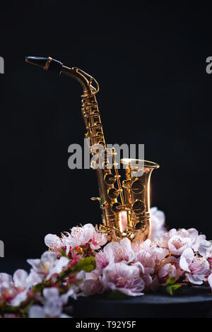 Winzige Saxophon mit rosa Kirschblüte auf einem dunklen Hintergrund mit kopieren. Frühjahr Musik Konzept. Stockfoto
